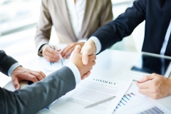 Image of business partners handshaking over business objects on workplace